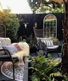 an outdoor seating area with chairs, pillows and plants on the ground in front of a black fence