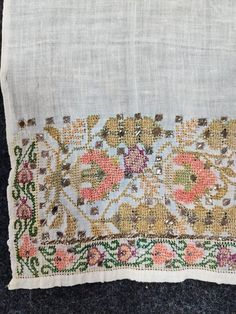 an embroidered piece of cloth with flowers and leaves on the edges, sitting on a black surface