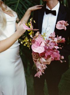 a man in a tuxedo holding a bouquet of flowers next to a woman in a white dress