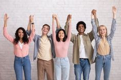 four people standing in front of a white brick wall with their hands up and arms raised