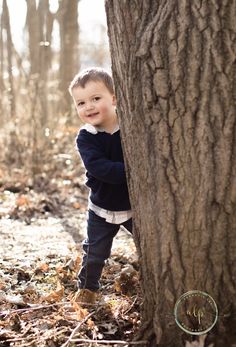 a little boy standing next to a tree in the woods with his arms wrapped around it