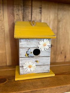 a birdhouse with white flowers painted on the sides and yellow roof, sitting on a wooden shelf