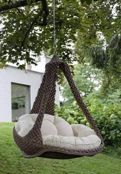 a brown and white swing chair hanging from a tree in front of a house on the grass