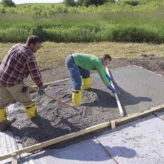 two men in yellow boots and green shirts are laying concrete on top of the ground