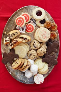 an assortment of cookies and pastries on a silver platter with red cloth in the background