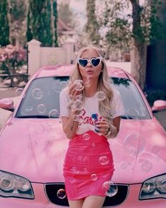 a woman is blowing bubbles in front of a pink car