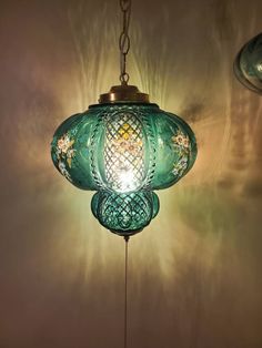 a green glass light hanging from the ceiling in front of a wall with two lights on it