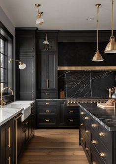 a large kitchen with black cabinets and marble counter tops, gold pulls on the handles