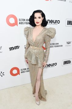 a woman in a long dress standing on a white carpet and posing for the camera