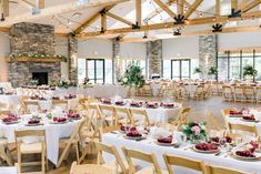 tables and chairs set up in a large room with wood beams, white tablecloths and greenery