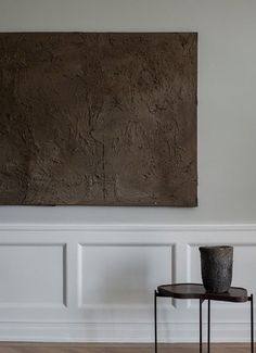 a table with a vase on it in front of a wall and a large painting