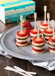 mini cheesecakes with strawberries are arranged on a silver platter next to a box of buttermilk pancake mix