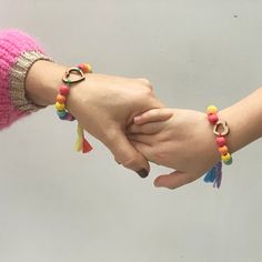 two people holding hands with colorful bracelets on their wrists and one wearing a pink sweater