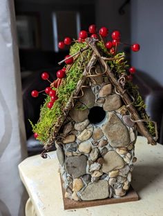 a bird house with moss and red berries on the roof is sitting on a table