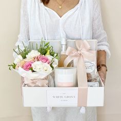 a woman holding a white box with flowers and personal care products in it's hands