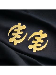 pair of gold earrings on black satin background with chinese symbol in the middle and two smaller letters