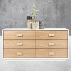 a white dresser with wooden drawers and vases on top