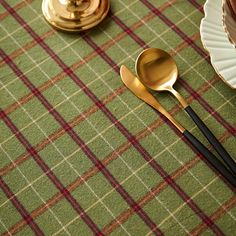 two gold spoons sitting on top of a green table cloth next to a plate