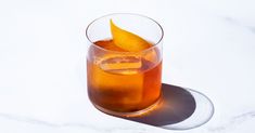 a glass filled with liquid and an orange peel on top of it, sitting on a white surface