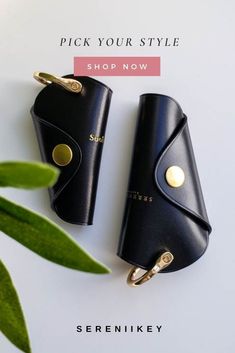 two black leather key fobs on top of a white table with green leaves