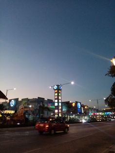 cars driving down the street at night in front of some stores and buildings with lights on them