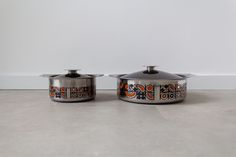 two pots with designs on them sit side by side in front of a white wall