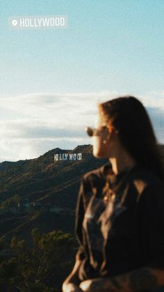 a woman standing on top of a hill looking at the sky and hills behind her