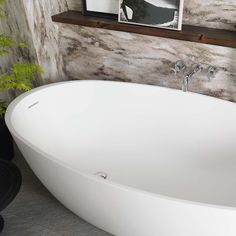 a large white bath tub sitting next to a wooden shelf with pictures on the wall