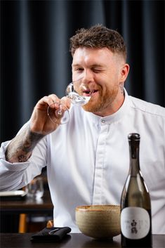 a man sitting at a table drinking from a wine glass while wearing a chef's uniform