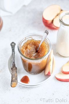 an apple pie in a glass jar on a plate next to sliced apples and a spoon