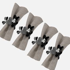 three black and white flowers are on the side of two gray napkins with silver ribbons