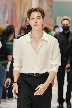 a young man in a white shirt and black pants is walking down the runway with his hand on his hip