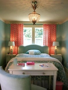 a bed sitting under a window in a bedroom next to a table with two lamps on it