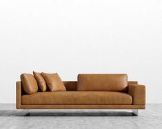 a tan leather couch sitting on top of a hard wood floor next to a white wall