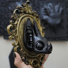 a person holding up a black and gold mirror with an animal's face in it