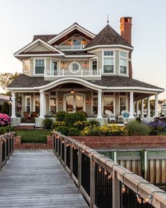 a large white house sitting on top of a lush green field next to a wooden bridge