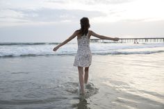 a woman is walking in the water at the beach with her arms spread wide open