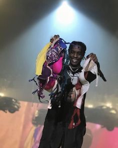 a man holding a bunch of clothes on top of his shoulders in front of a stage