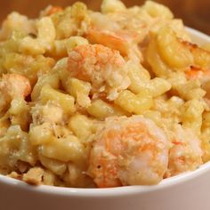 a white bowl filled with macaroni and cheese covered in shrimp, carrots and broccoli