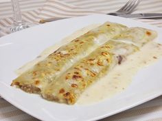 two enchiladas are sitting on a white plate next to a fork and knife