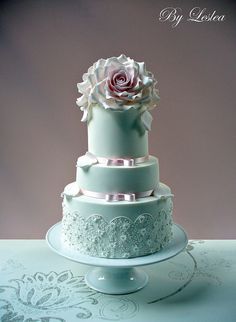 a three tiered wedding cake with a pink rose on the top and white lace