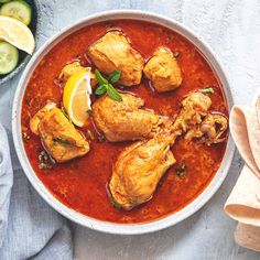 a bowl filled with chicken and sauce next to cucumbers