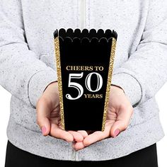 a person holding up a black and gold card with the words cheers to 70 years on it