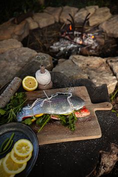 a fish sitting on top of a cutting board next to some lemons and herbs