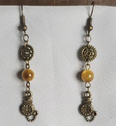 Steampunk dangle earrings made of bronze clock and gear charms & findings. Golden tiger's eye beads. Perfect to accent your cosplay, show off at a convention, or just wear in everyday life! Handcrafted in Tucson, Arizona! Bead color may seem different/darker when not under the blazing Arizona sun. Handmade Steampunk Gold Jewelry, Steampunk Dangle Earrings For Pierced Ears, Gold Steampunk Dangle Jewelry, Handmade Gold Steampunk Earrings, Gold Steampunk Necklace Vintage, Golden Tiger, Steampunk Clock, Spike Earrings, Tiger Eye Beads