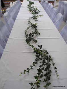 the long table is covered with white linens and greenery, as well as flowers