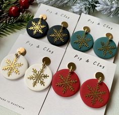 four different colored snowflake earrings on top of a card next to a christmas tree