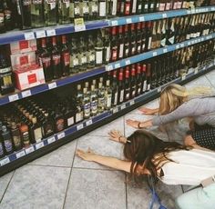 two women are sitting on the floor in front of shelves with alcohol bottles and liquor