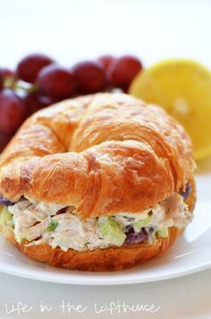 a croissant sandwich with chicken salad on it next to grapes and lemons