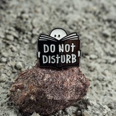 a black and white pin with the words do not disturb on it sitting on top of a rock